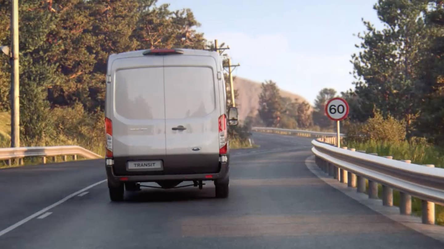 Vue arrière du Ford Transit sur route à proximité d’un panneau de signalisation.