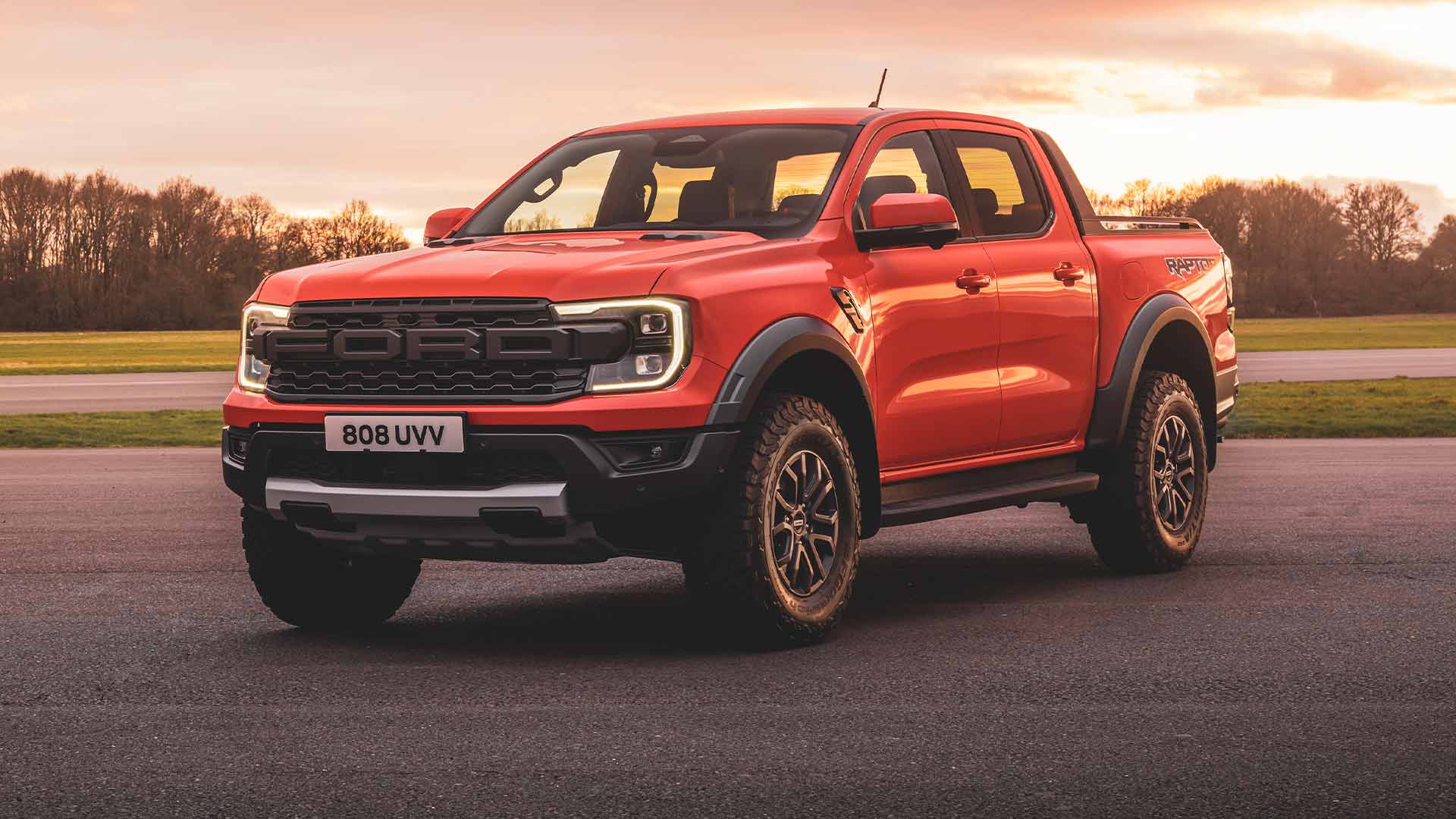 Ford Ranger Raptor Code Orange garé sur une piste avec les phares allumés. 