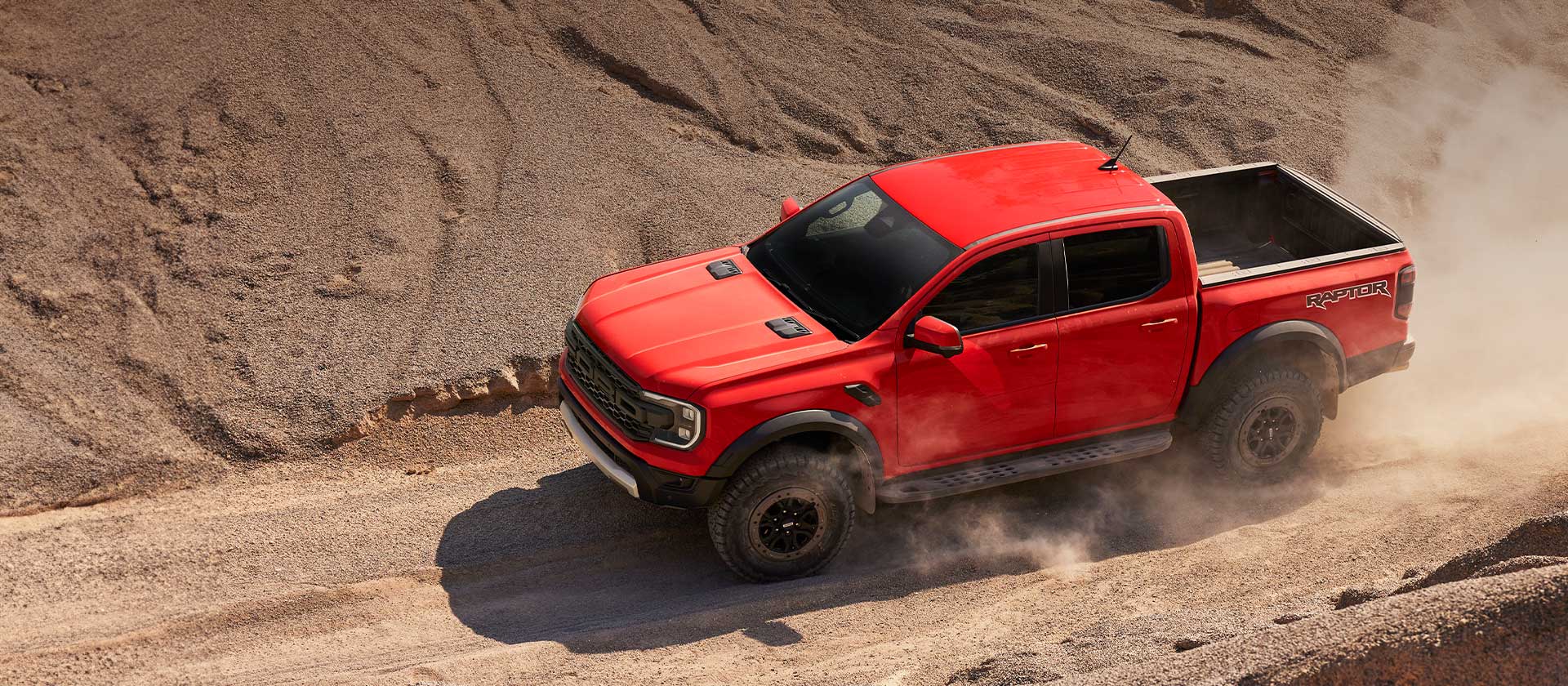 Ford Ranger Raptor Code Orange en montée dans la poussière.