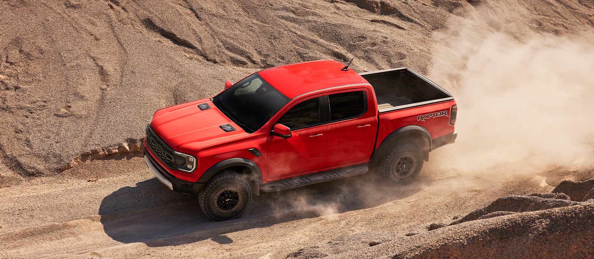 Ford Ranger Raptor Code Orange en montée dans la poussière.