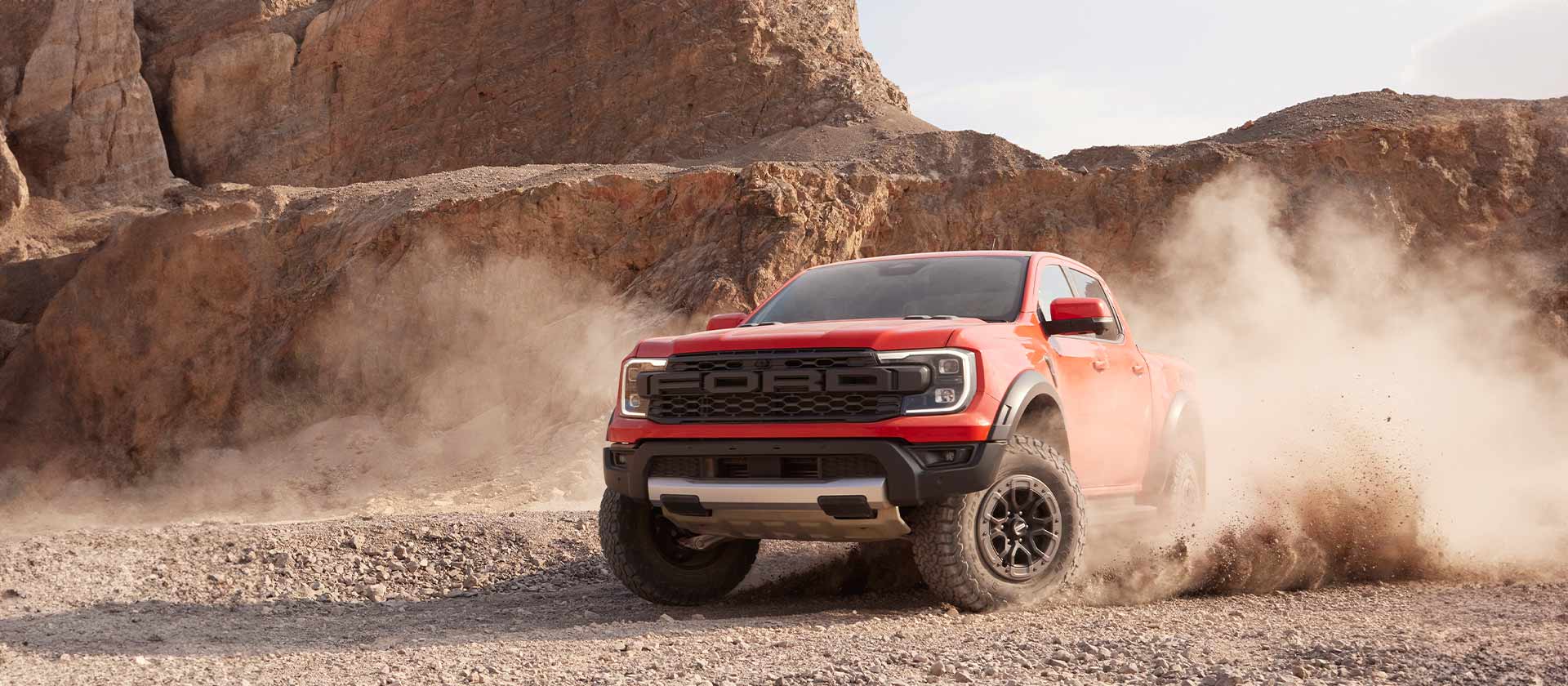 Ford Ranger Raptor Code Orange conduisant à travers la poussière de roche concassée.