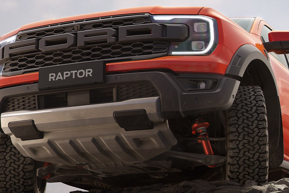 Face avant inférieure d’un Ford Ranger Raptor Code Orange montrant la suspension et la calandre. 