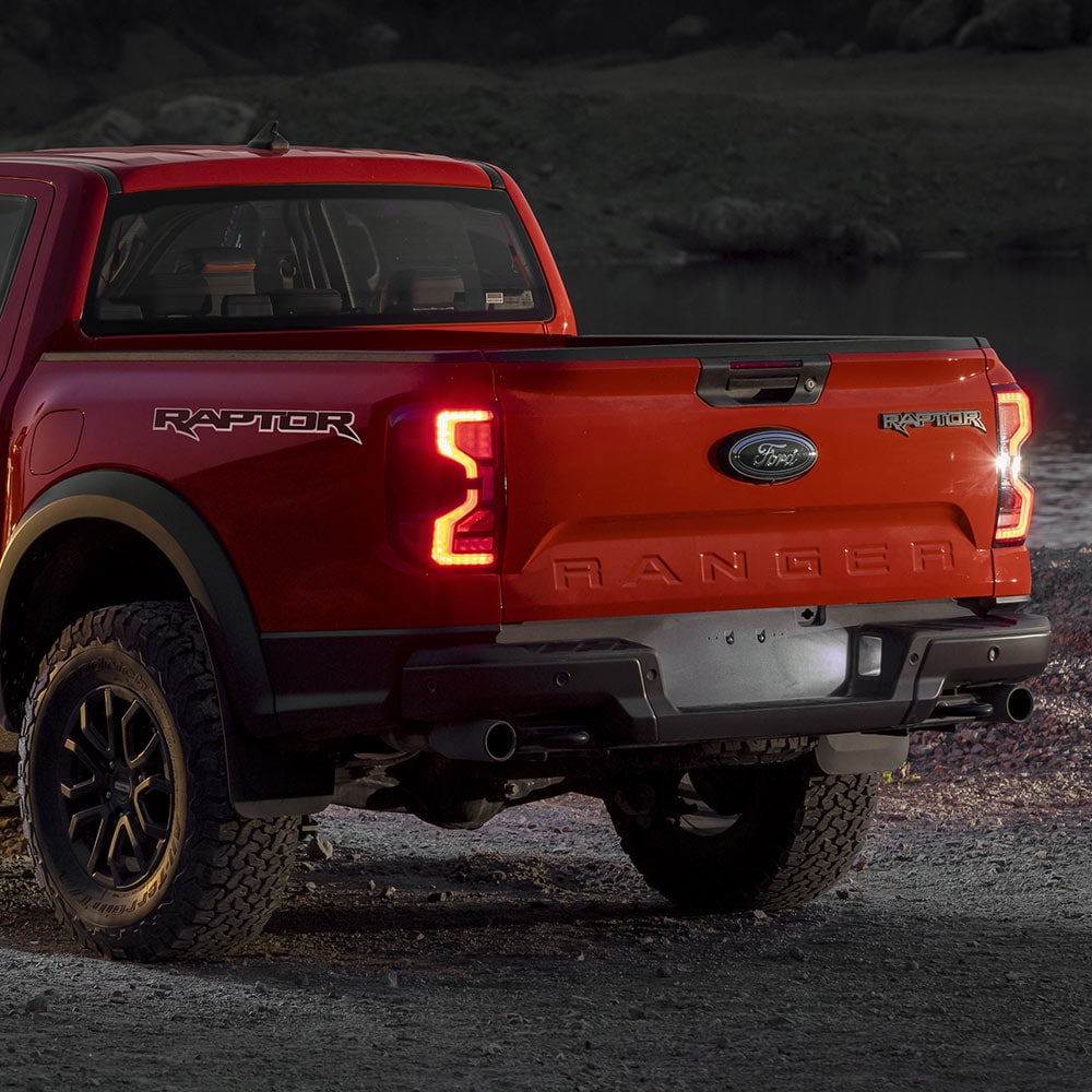 Vue arrière d’un Ford Ranger Raptor Code Orange avec feux arrière allumés.
