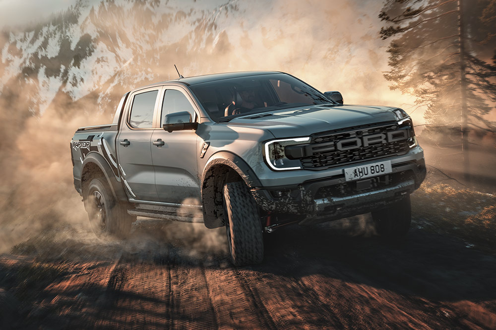 Ford Ranger Raptor en mode Baja roulant sur un chemin de terre, avec un paysage montagneux en arrière‑plan.