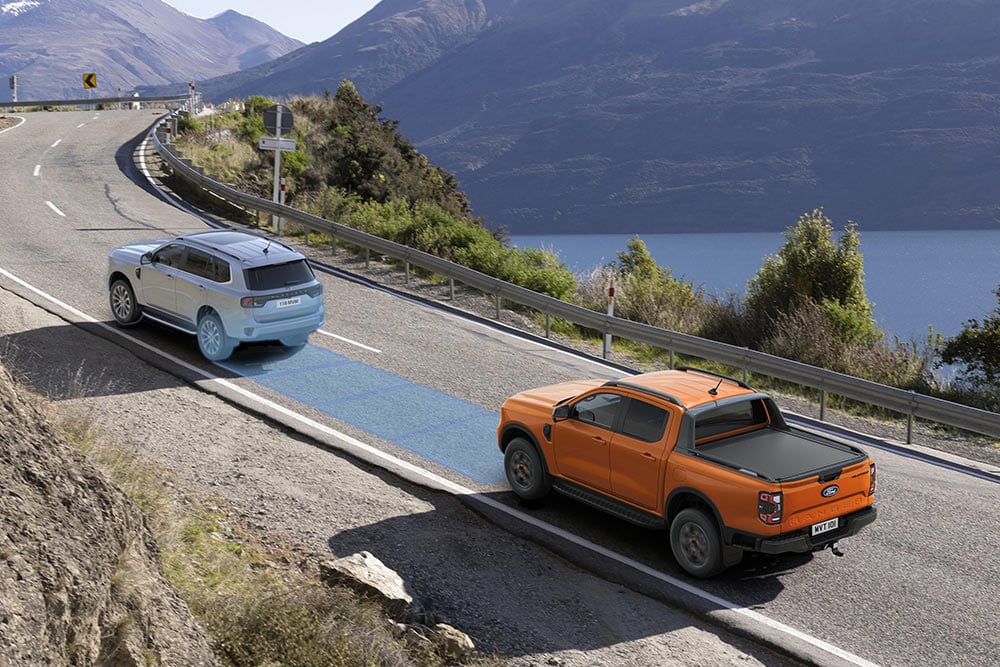 Ford Ranger Raptor jaune roulant sur une route de montagne pittoresque, mettant en avant les systèmes d’aide à la conduite du véhicule.