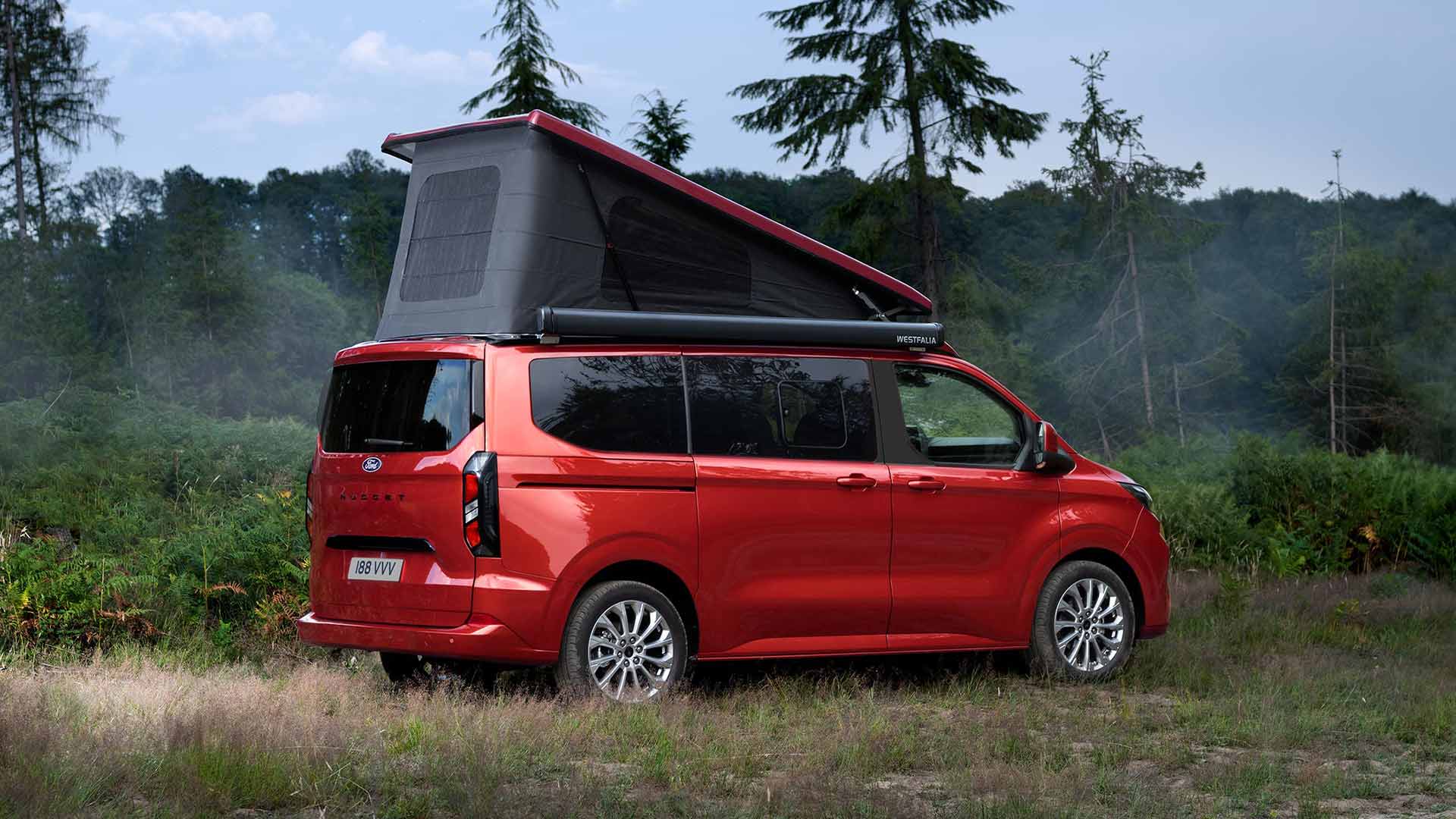 Ford Transit Custom Nugget rouge, avec le toit relevable à toile repliable déployé, garé dans un pré.