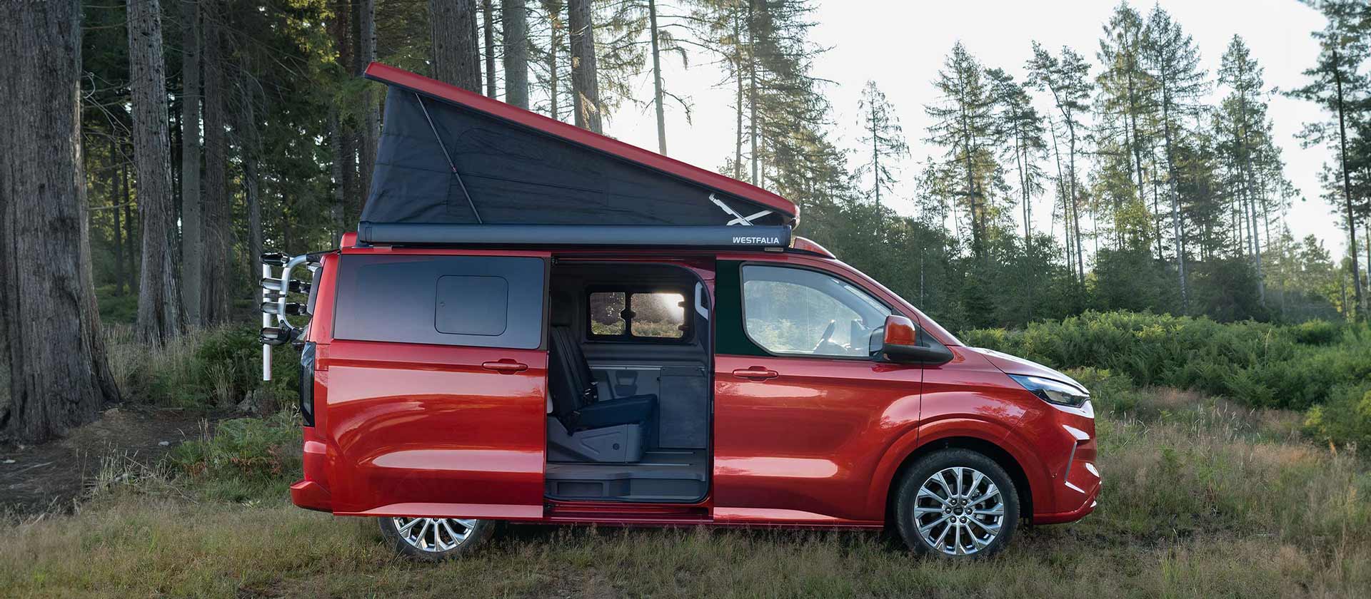 Ford Transit Custom Nugget rouge garé avec le toit relevable à toile repliable déployé et la porte latérale coulissante ouverte.