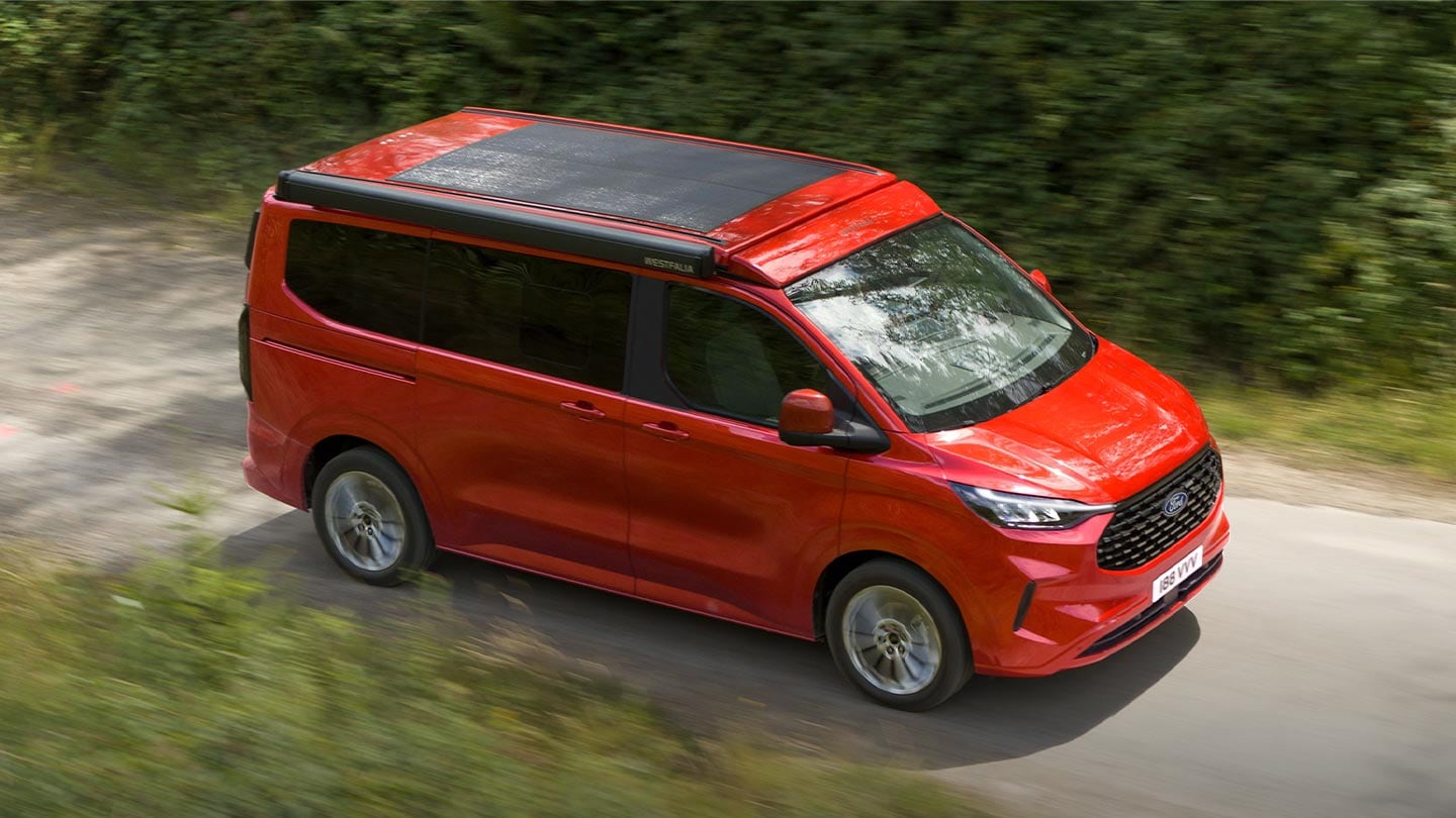 Ford Transit Custom Nugget rouge roulant sur un chemin de terre.