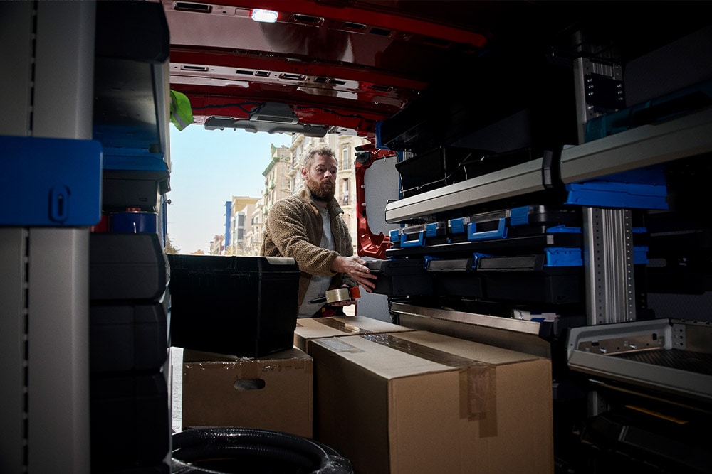 Un livreur déchargeant des colis par la porte latérale d'un Ford Transit Custom rouge.