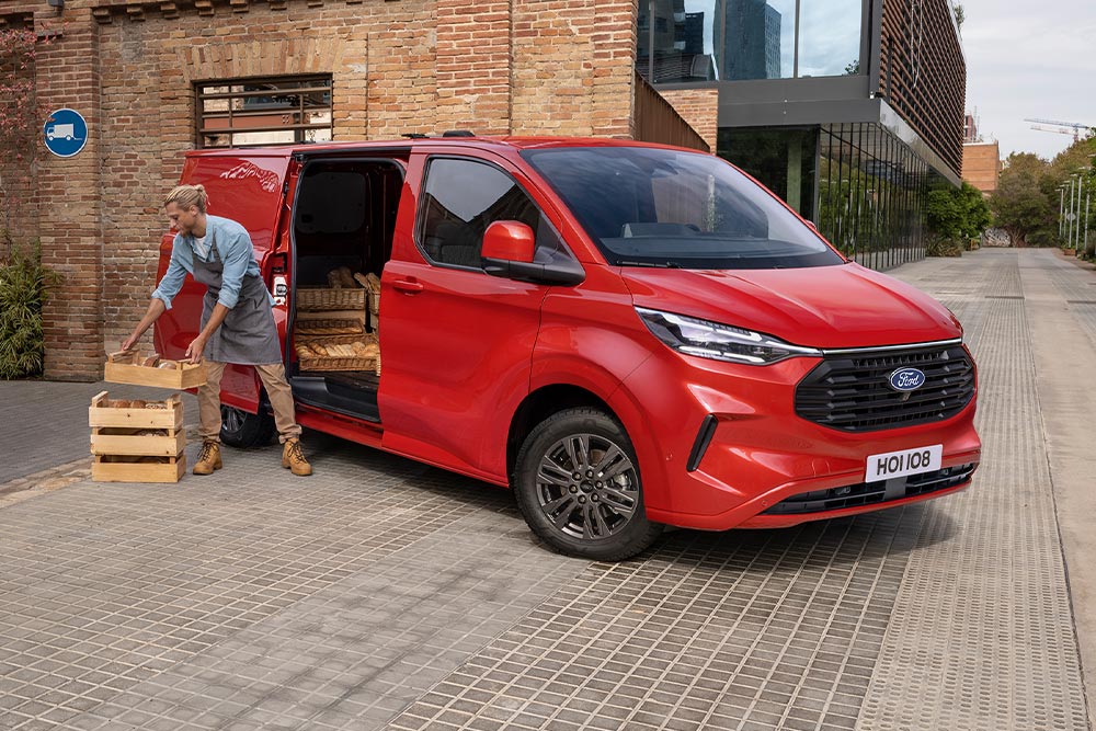 Un livreur charge des colis dans un Ford Transit Custom rouge.