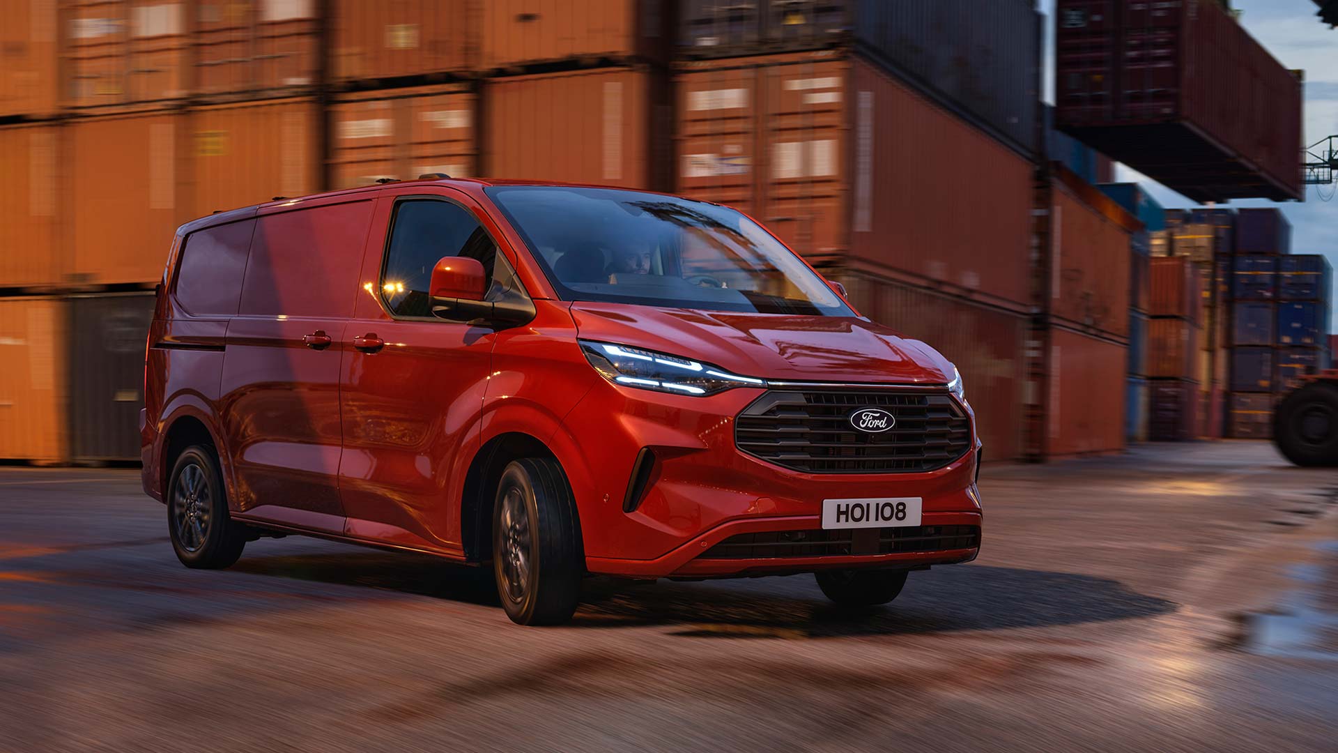 Un fourgon Ford Transit Custom rouge roule sur les quais d'un port. 
