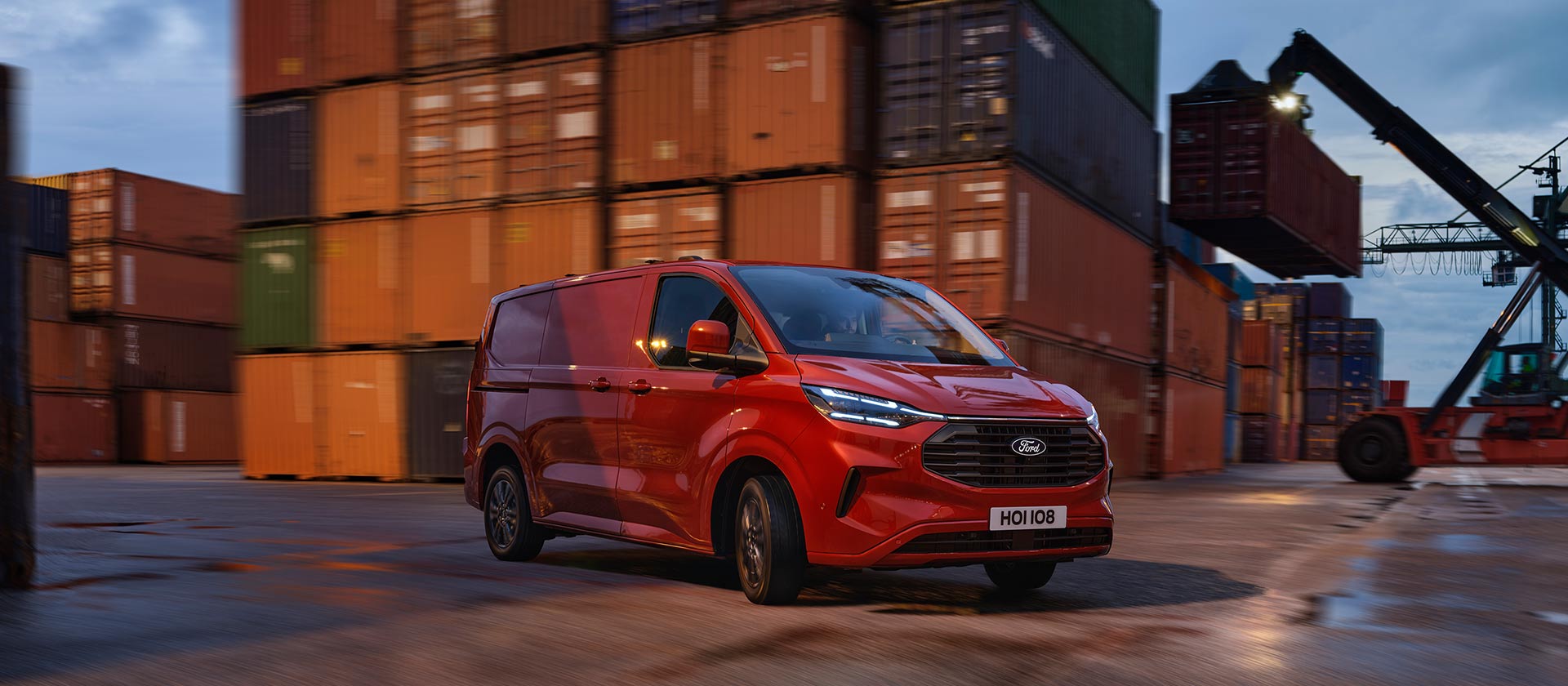 Un fourgon Ford Transit Custom rouge roule sur les quais d'un port.