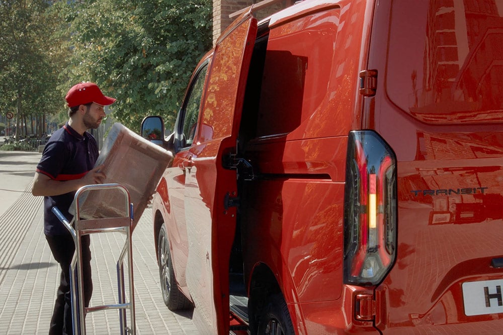Un livreur décharge des colis d'un Ford Transit Custom rouge.