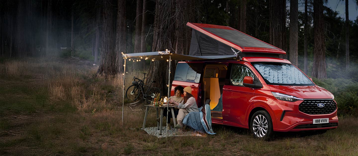 Camping-car Ford Transit Custom Nugget rouge stationné dans une forêt.