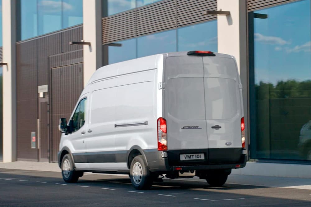 Vue arrière d’un fourgon Ford Transit blanc stationné dans une rue.