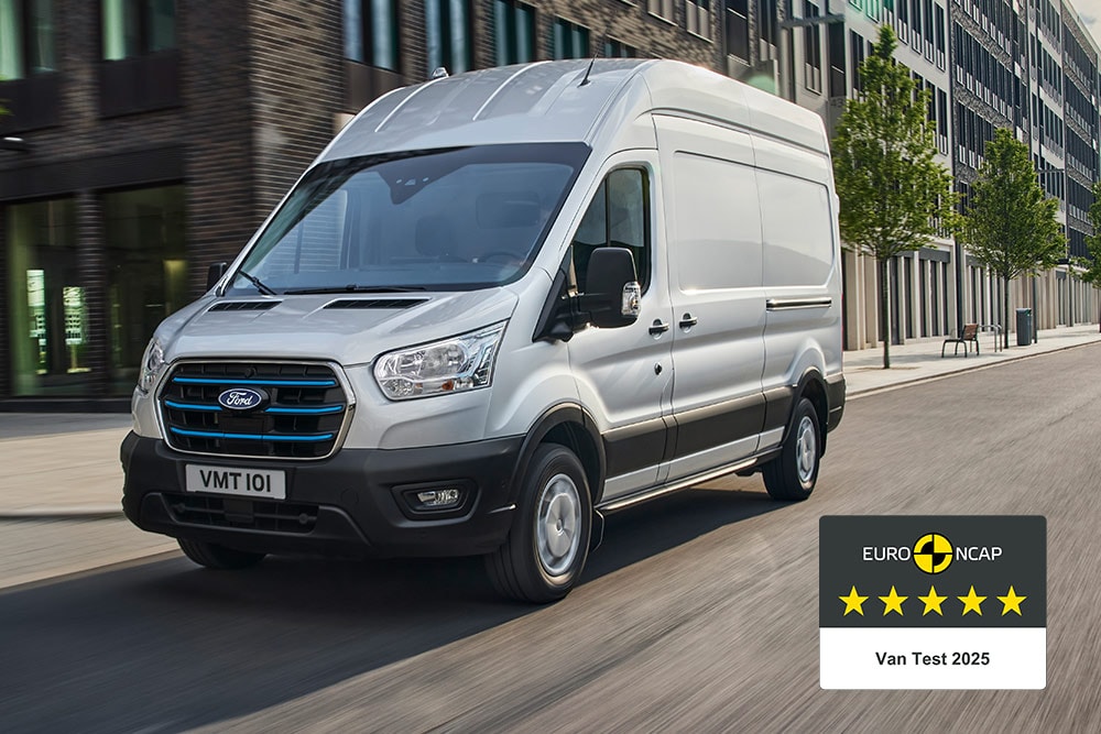 Un fourgon électrique E-Transit Ford argenté circule sur une route, arborant une vignette « Gold 2022 Commercial Van Safety » (Médaille d’or 2022 pour la sécurité des véhicules utilitaires).