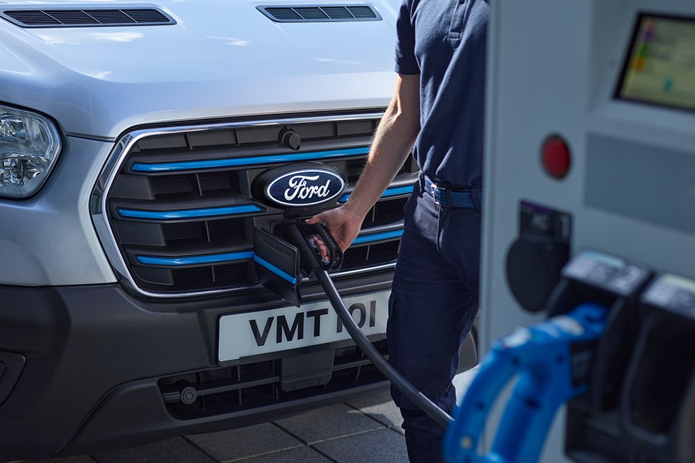 Gros plan d’une personne qui branche un câble de recharge sur un fourgon électrique Ford E-Transit argenté.
