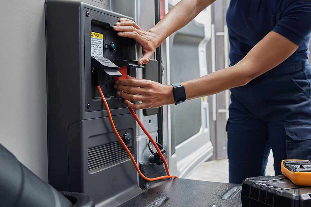 Gros plan d’une personne qui branche un câble de recharge à l’intérieur d’un fourgon électrique E-Transit Ford.