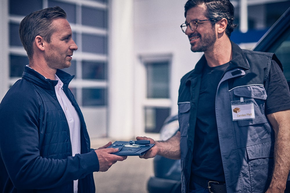 Man handing a tablet to another man in front of a Ford Transit van.