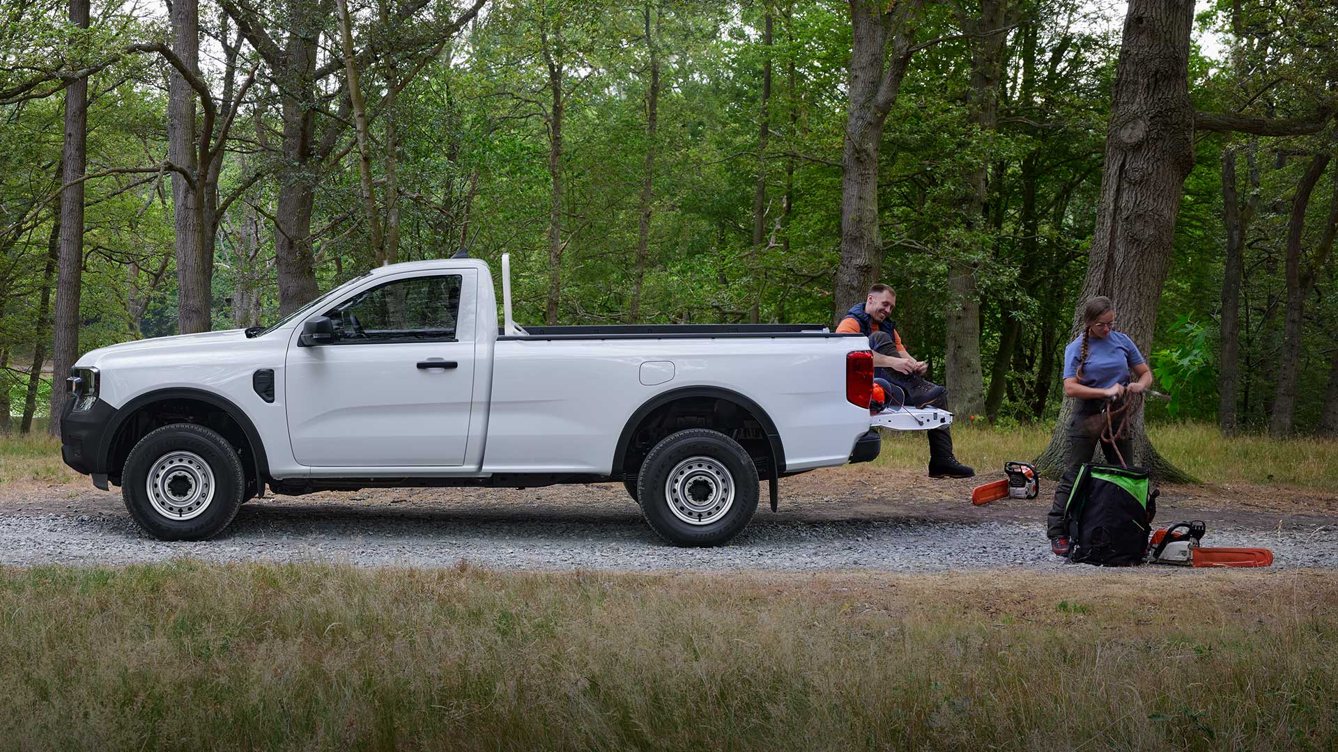 Vue de côté du Ford Ranger Simple Cabine blanc, garé en forêt, avec deux personnes déchargeant du matériel à l’arrière.