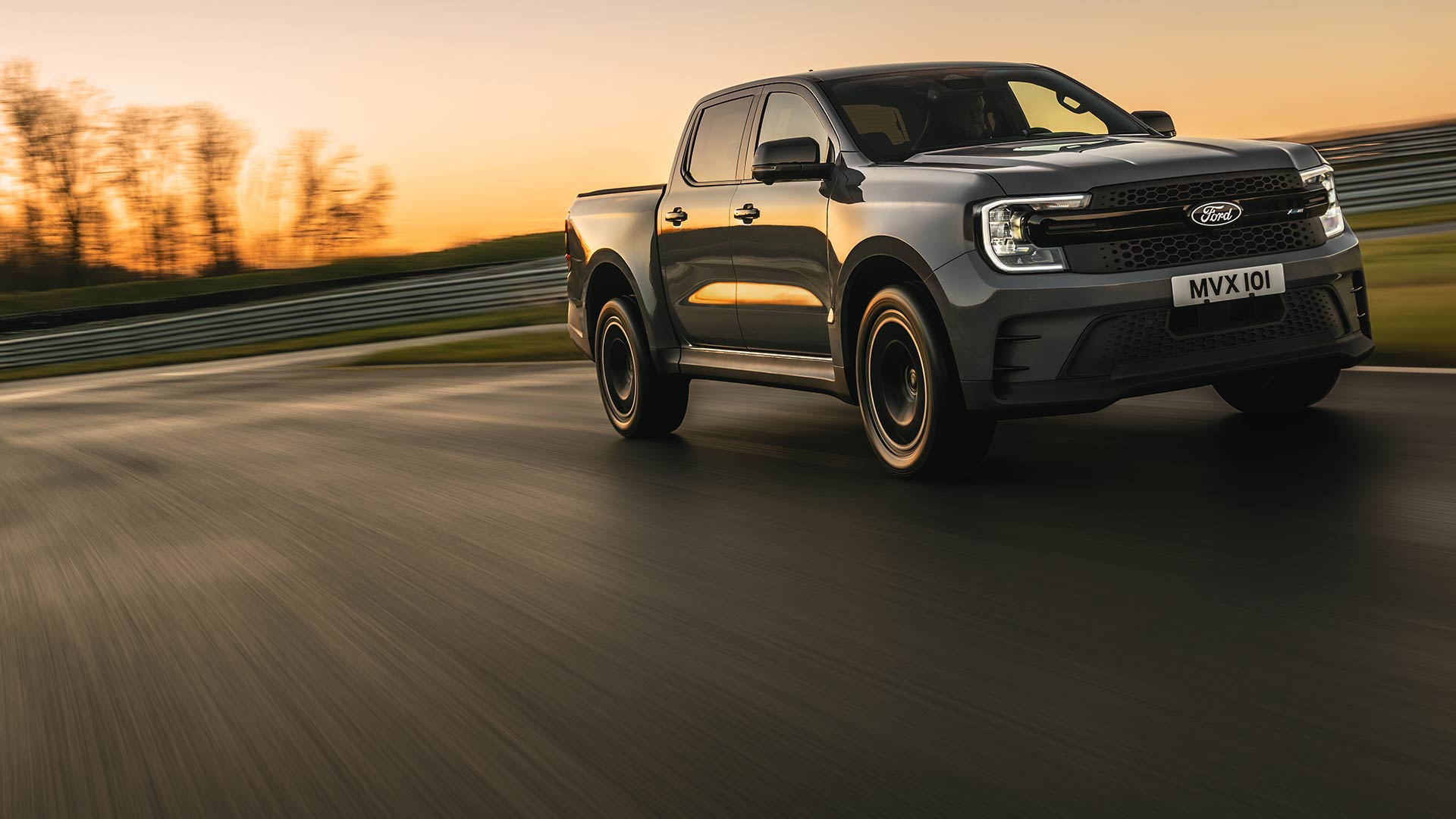 A dark gray Ford Ranger Platinum drives on a track at sunset.