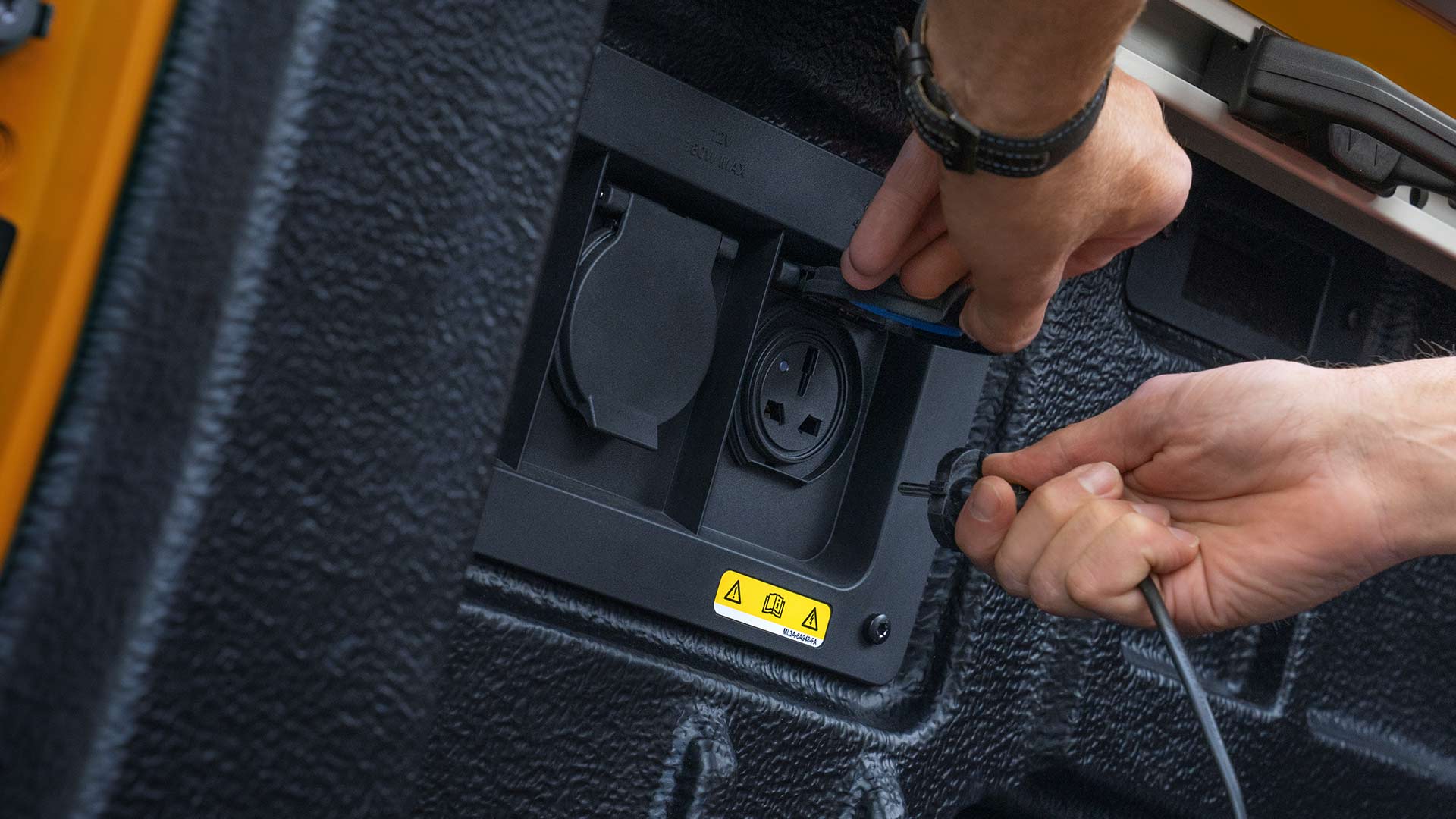 Gros plan sur des mains qui branchent des câbles à la prise électrique du plateau de chargement du Ford Ranger.