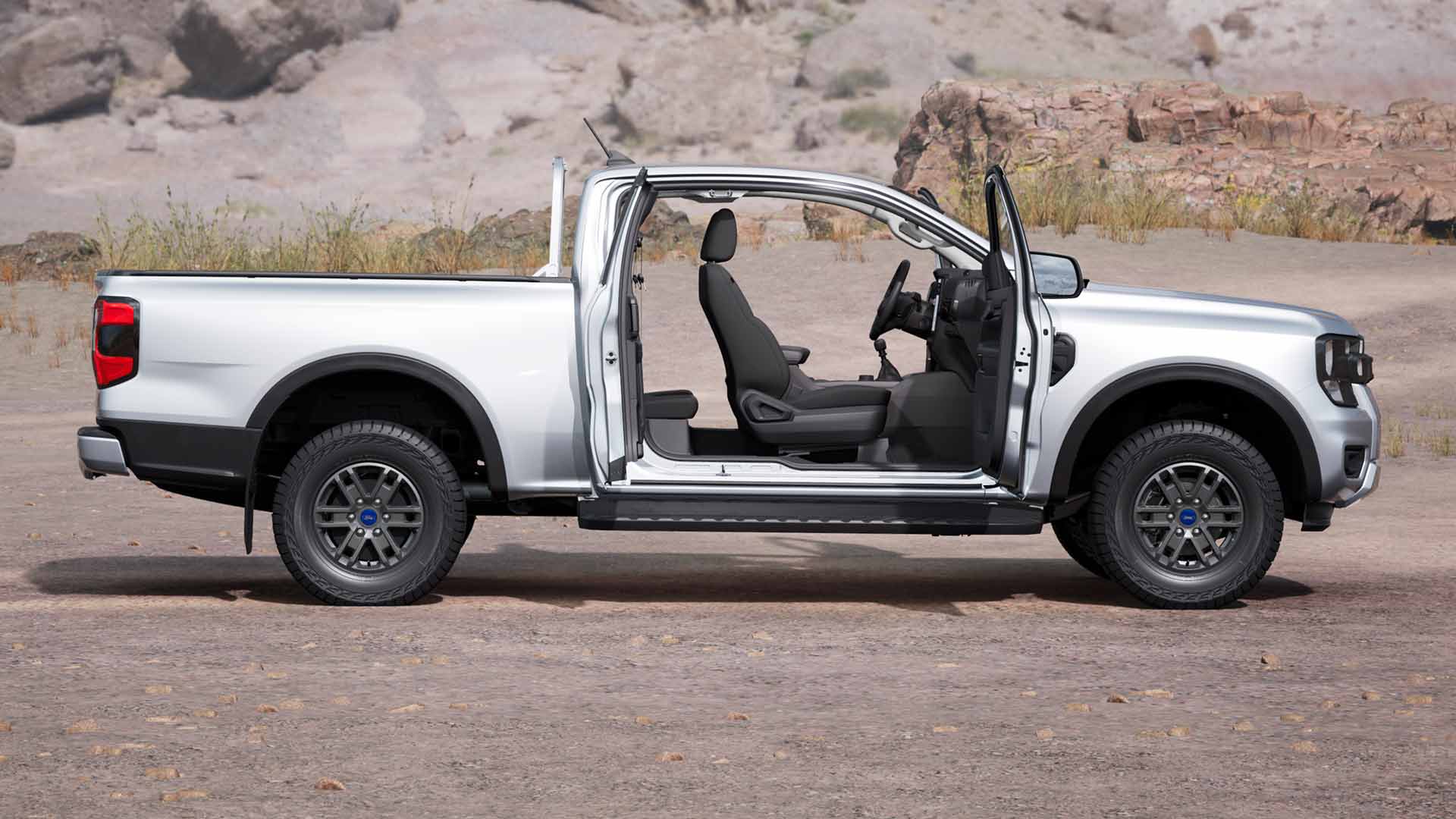 Profil d’un Ford Ranger XLT Super Cab argenté, portes ouvertes, garé sur un terrain poussiéreux.