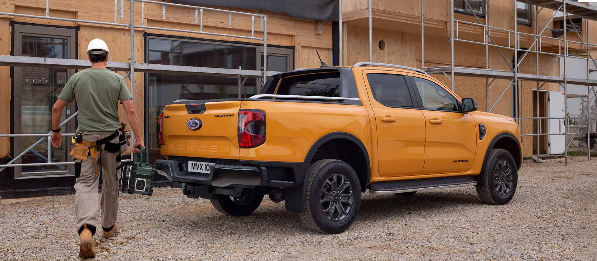 Un travailleur portant un casque de chantier s’approche d’un pick-up Ford Ranger jaune sur un chantier.
