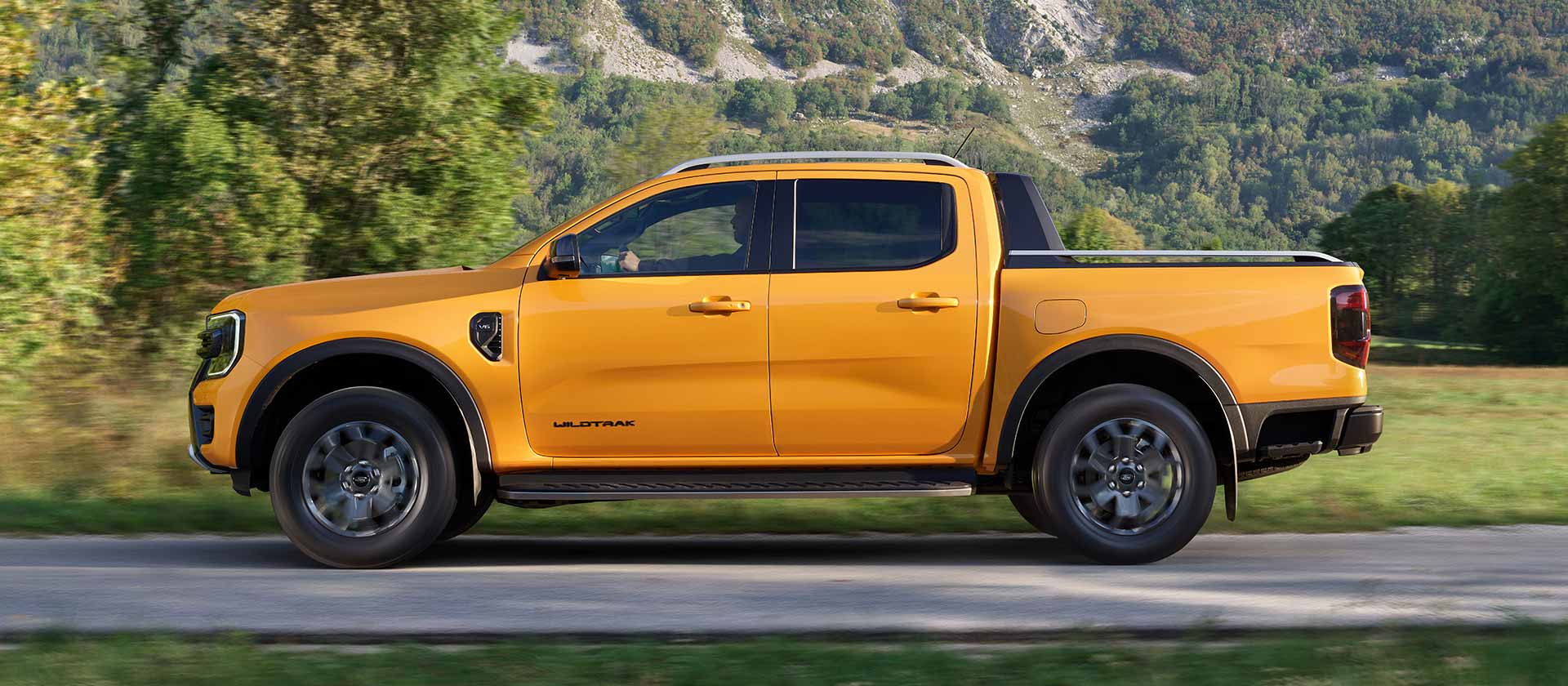 Vue latérale d’un Ford Ranger Wildtrak jaune roulant sur une route goudronnée.