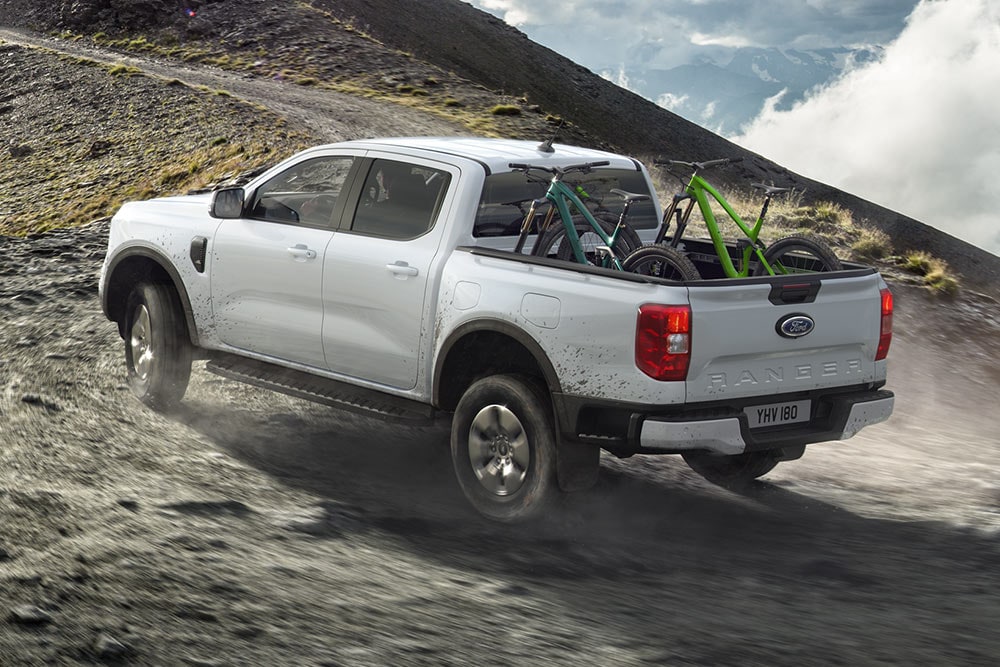 Un Ford Ranger Stormtrak PHEV roule hors route sur une colline, deux vélos sont chargés dans l’espace de stockage.