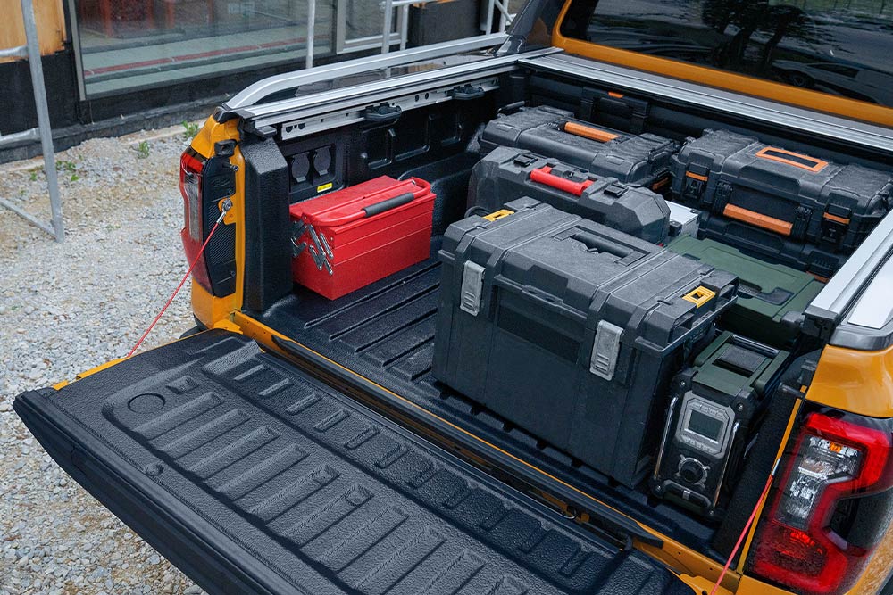 Le hayon d’un Ranger jaune est abaissé, une planche de bois y est fixée par une pince.