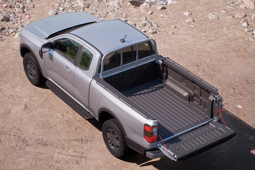 Ford Ranger XLT Super Cab argenté garé sur une surface sablonneuse, hayon ouvert, vu de dessus.