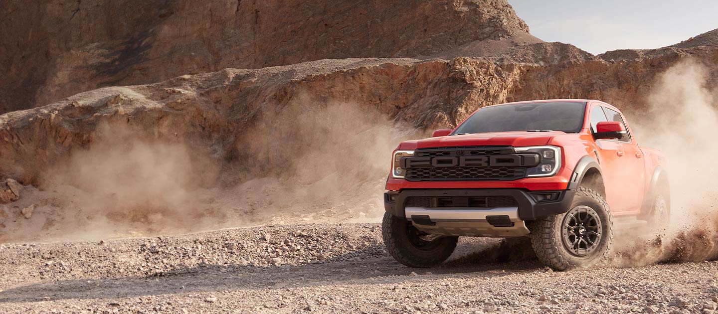 Un Ford Ranger Raptor rouge soulève la poussière en traversant un paysage désertique.