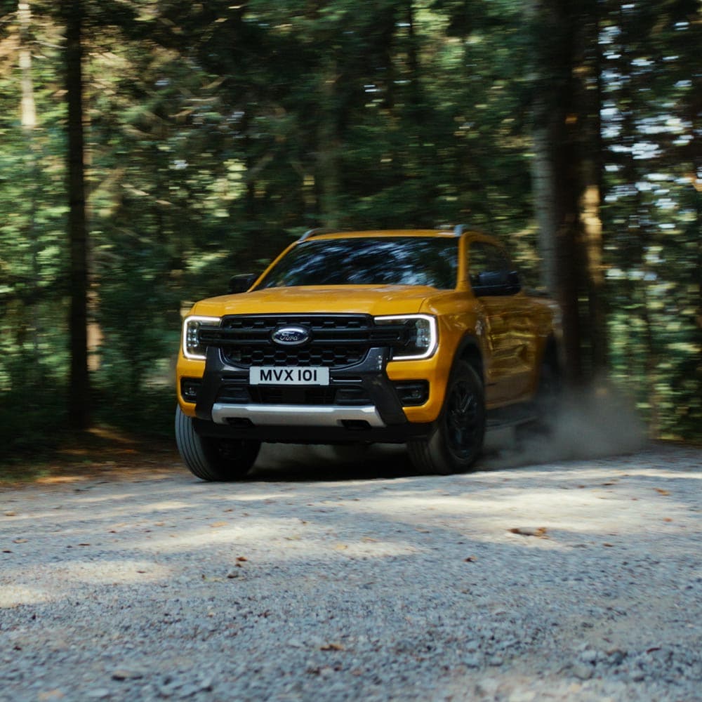 Yellow Ford Ranger driving on a forest trail.