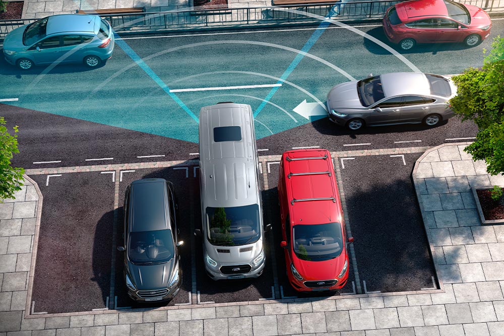 Fourgon Ford Transit argenté en marche arrière, avec des lignes bleues indiquant l’utilisation des capteurs de stationnement arrière.