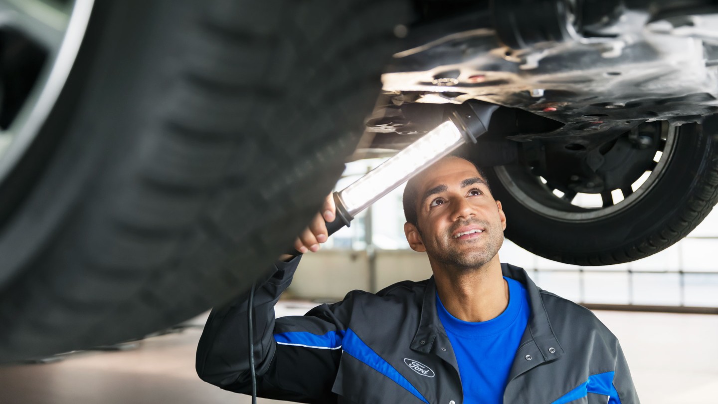 Un technicien Ford Service en train d’inspecter le dessous d’un utilitaire.