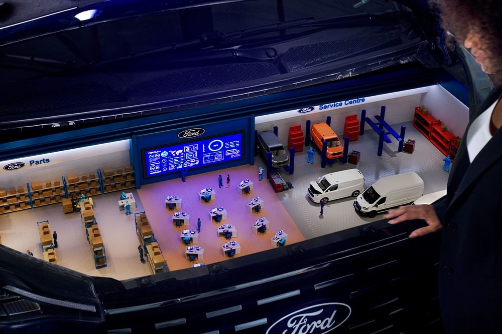 Miniature model of Ford Pro service ecosystem displayed inside a vehicle grille showing parts, service bays, and a digital uptime monitoring screen.