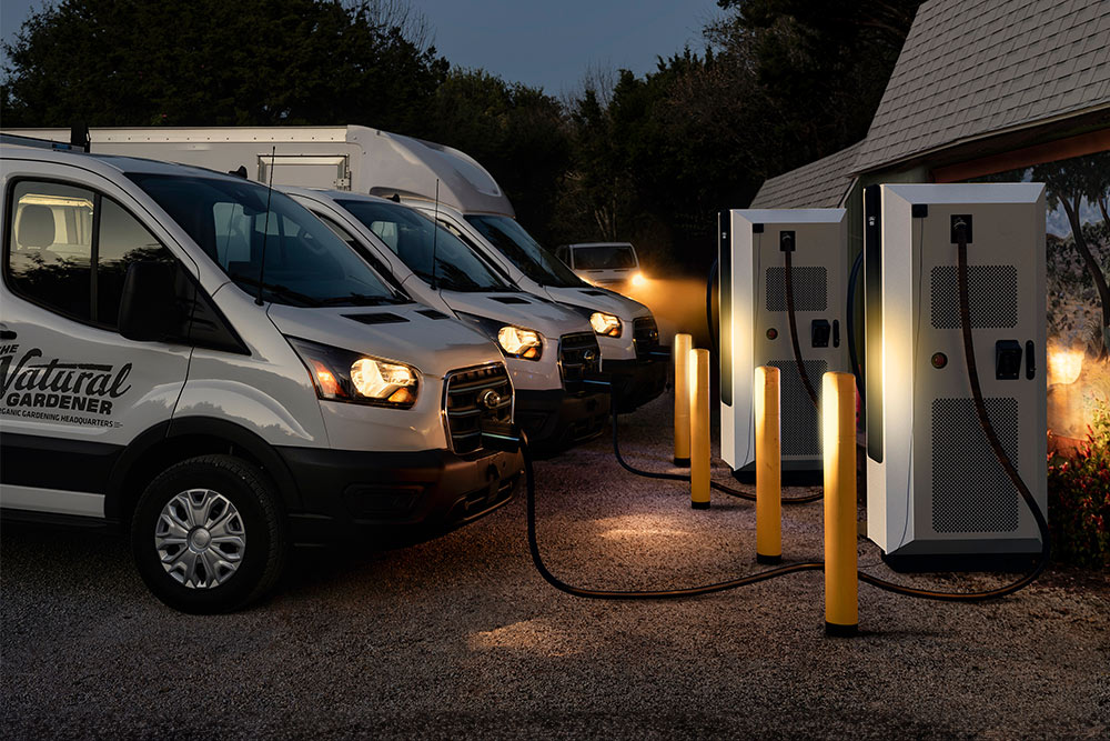 Scène de soirée de fourgons électriques Ford en charge à une station électrique.