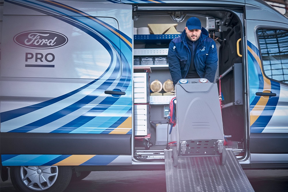 Un technicien mobile Ford Pro sort des outils d'une camionnette Transit devant une entreprise.