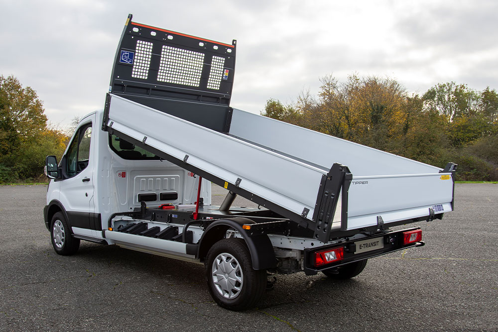 Châssis-cabine Ford Pro blanc avec plateau surélevé garé sur un parking pavé.