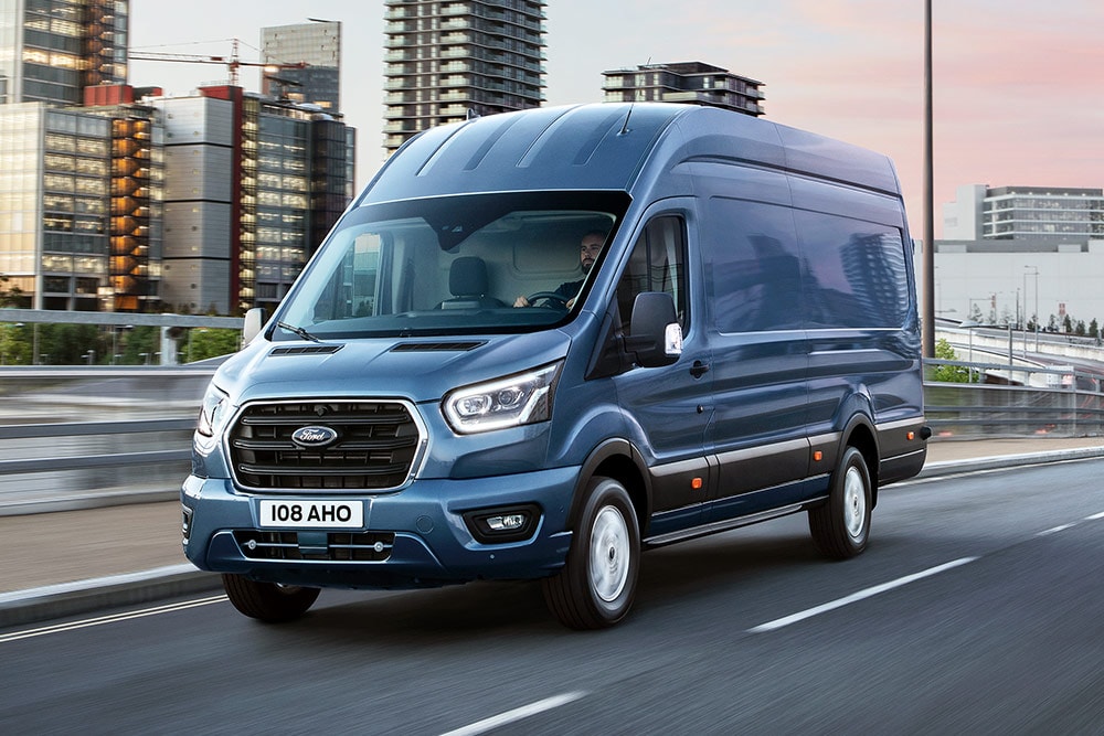 Un Ford Transit traversant un pont, avec un paysage urbain dense en arrière-plan.