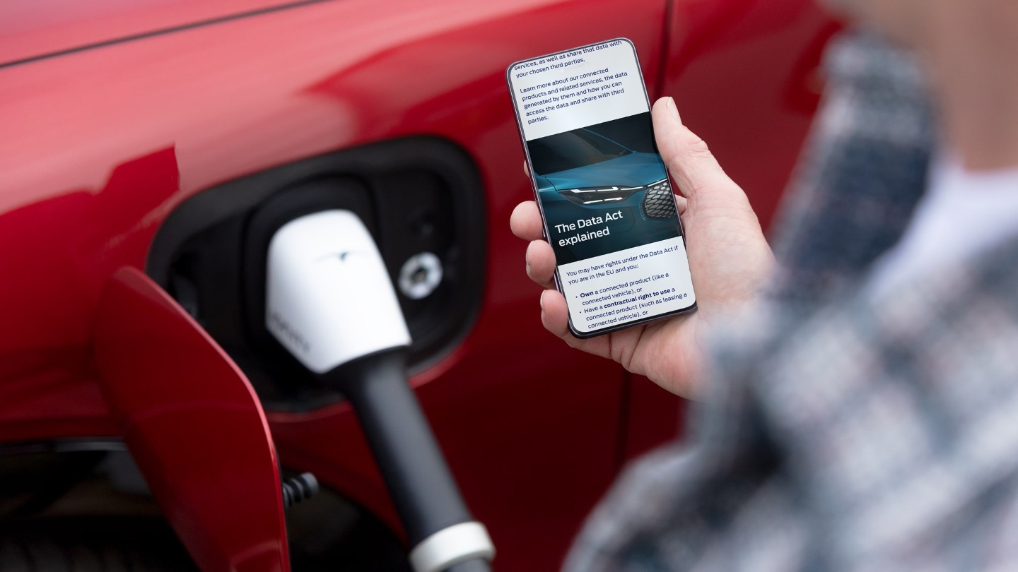 Une personne vérifiant son smartphone, un véhicule électrique rouge en charge en arrière-plan.