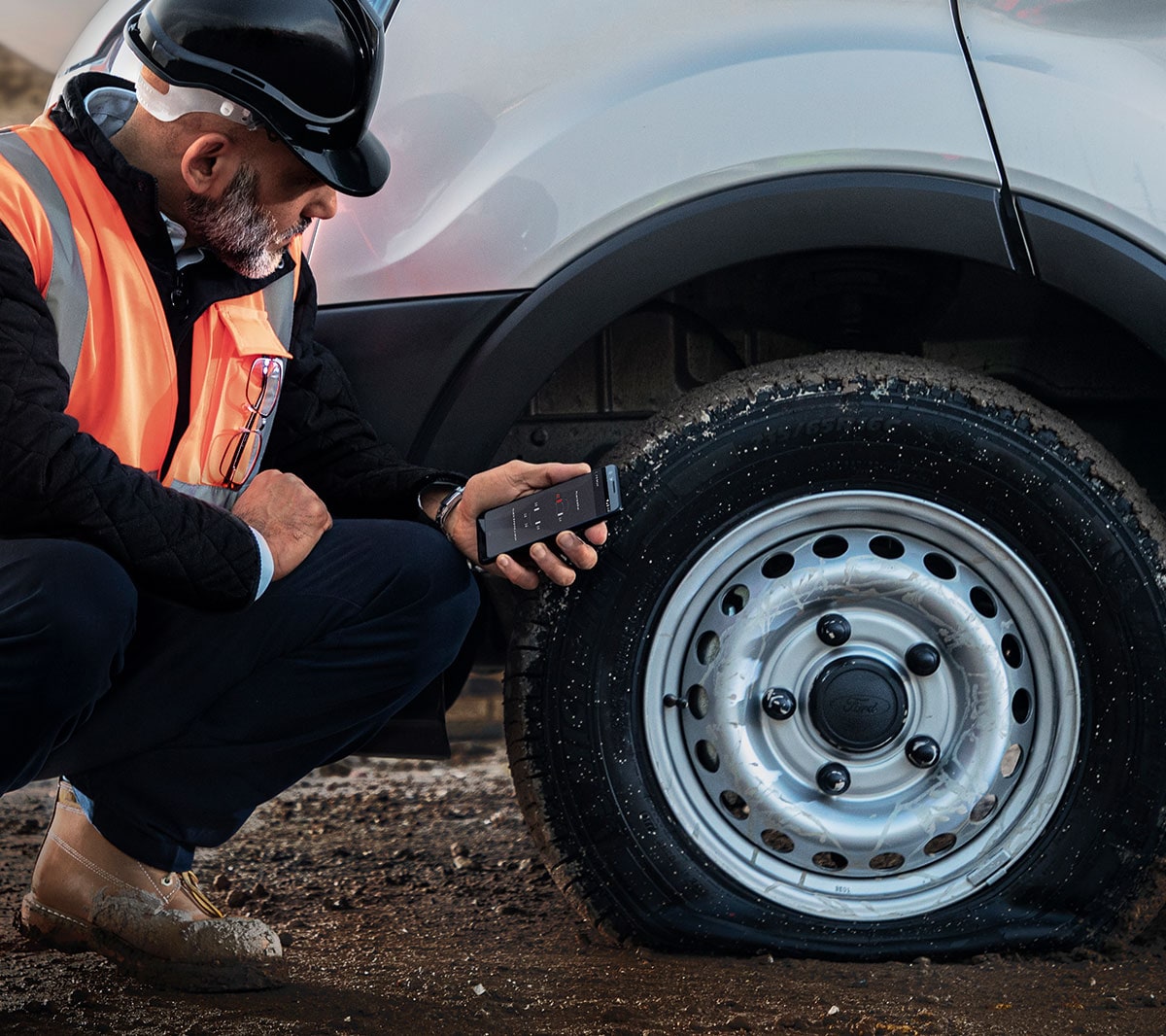 Un travailleur de la construction en veste à haute visibilité inspectant un pneu plat.