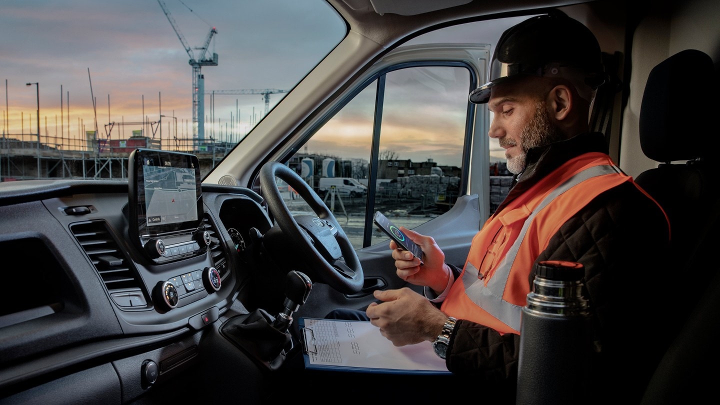 Un travailleur de la construction en veste à haute visibilité assis sur le siège avant d’un fourgon Ford Transit.