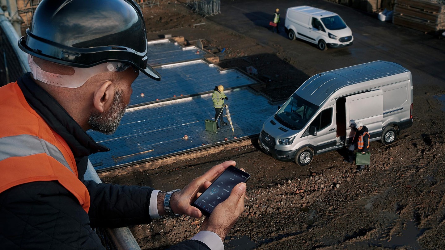 Une personne en veste à haute visibilité regardant le chantier où se trouve un fourgon Ford.