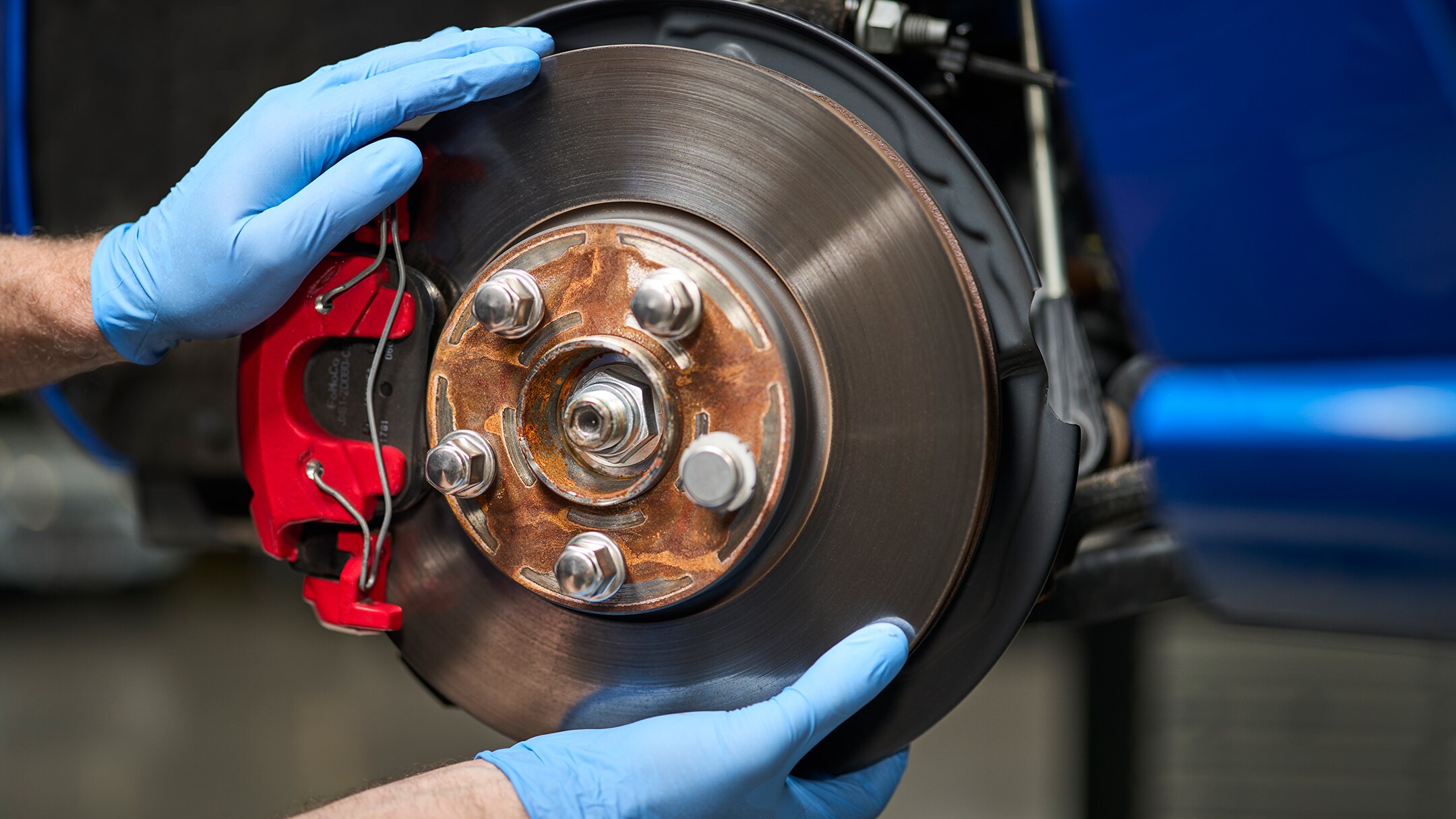 Un mécanicien portant des gants bleus installe un nouveau disque de frein sur une voiture bleue.