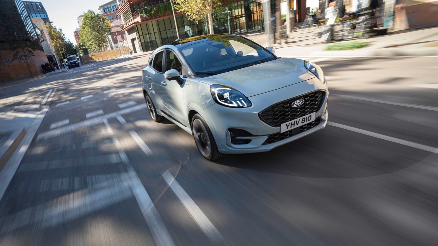 Un véhicule Ford Puma gris clair en mouvement dans une rue de la ville.