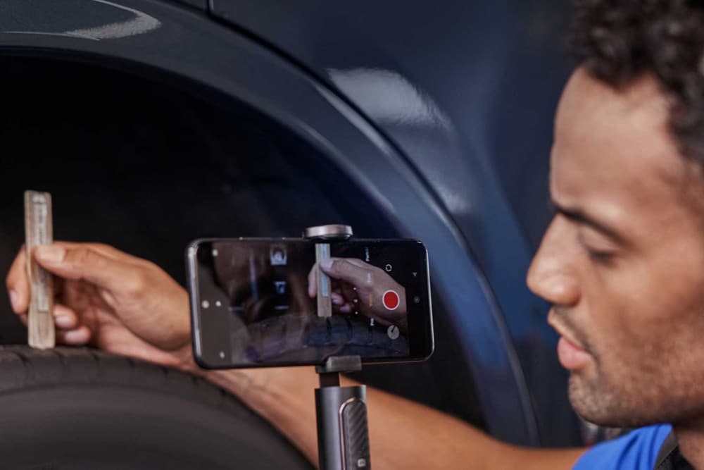 Un technicien filme un pneu avec un smartphone monté sur trépied pour un contrôle vidéo.