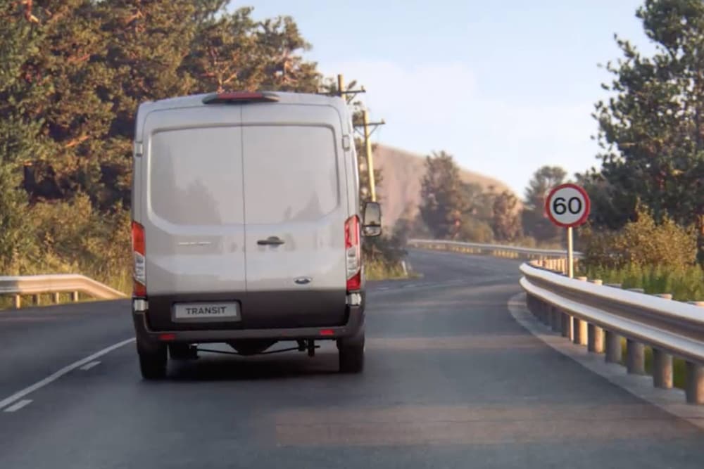 Le Ford Transit 2T vu de dos roulant sur la route avec un panneau de signalisation