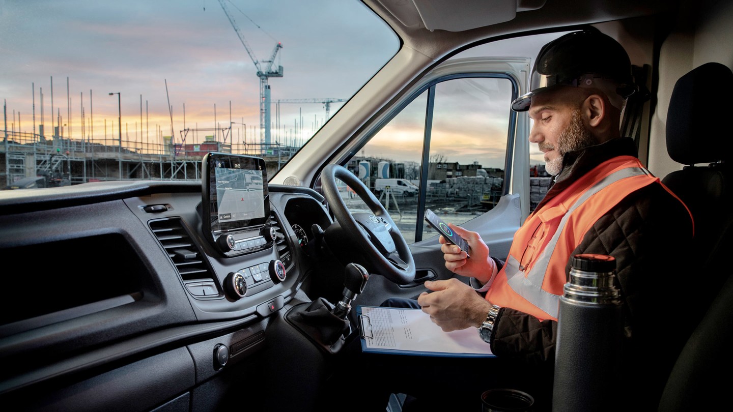 Un dépanneur Ford consultant son téléphone dans un Ford Transit.